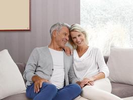 [Translate to Französisch:] Altere Paar auf Couch mit Infrarotheizung an der Wand
